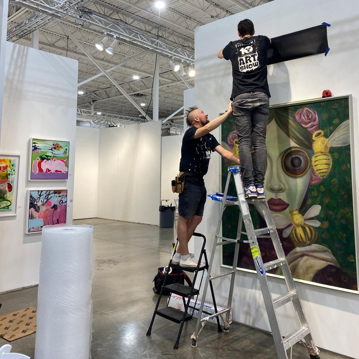 Two art handlers installing a large painting at an art fair