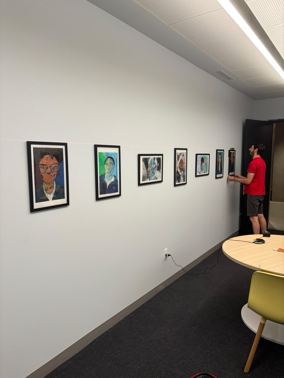 An art handler installing a receding row of framed portraits down a corridor